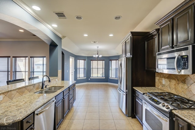 kitchen with dark brown cabinetry, sink, light stone counters, pendant lighting, and stainless steel appliances