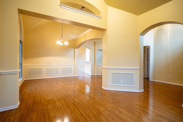 empty room featuring hardwood / wood-style flooring, ornamental molding, high vaulted ceiling, and a chandelier