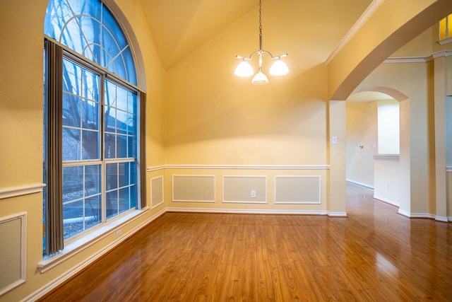 empty room featuring an inviting chandelier, a wealth of natural light, wood-type flooring, and vaulted ceiling