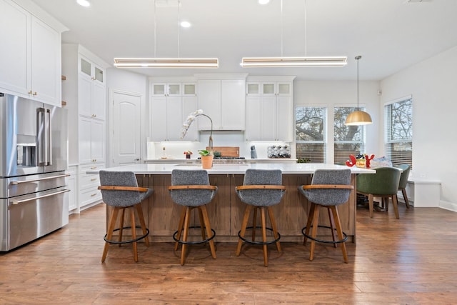 kitchen with pendant lighting, a kitchen island with sink, high end refrigerator, and white cabinets