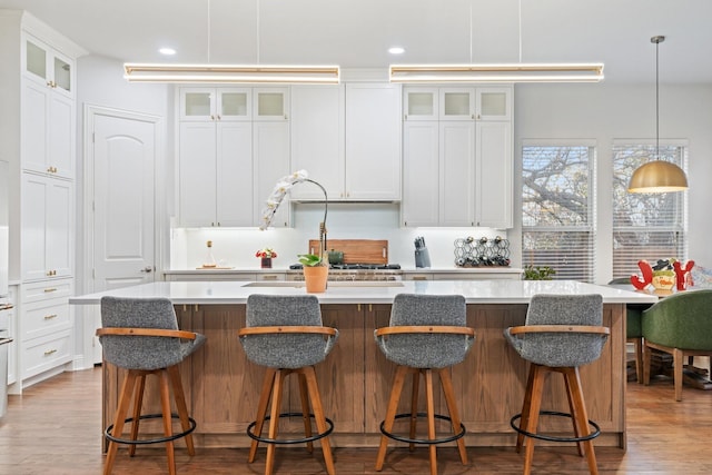 kitchen featuring a large island with sink, pendant lighting, white cabinets, and a kitchen breakfast bar