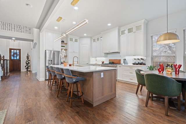 kitchen with stainless steel refrigerator with ice dispenser, dark wood-type flooring, white cabinetry, hanging light fixtures, and a center island with sink