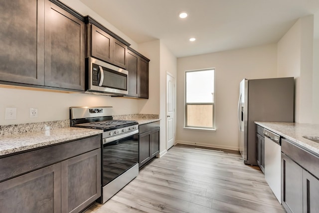 kitchen featuring dark brown cabinetry, light stone countertops, light wood-type flooring, and appliances with stainless steel finishes