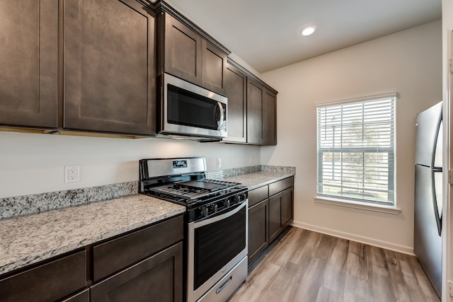 kitchen featuring light stone countertops, dark brown cabinets, light wood-type flooring, and appliances with stainless steel finishes