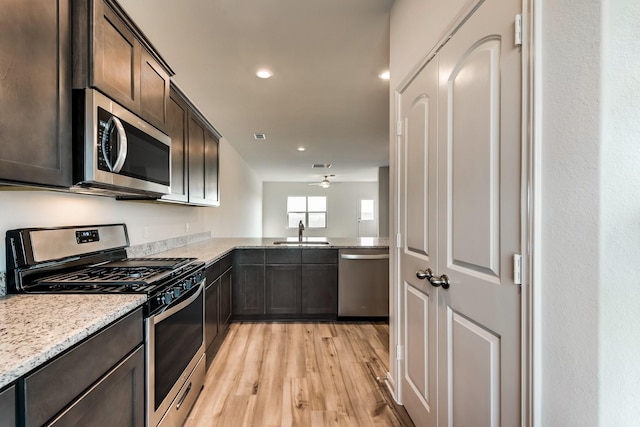 kitchen with appliances with stainless steel finishes, dark brown cabinetry, ceiling fan, sink, and light hardwood / wood-style flooring