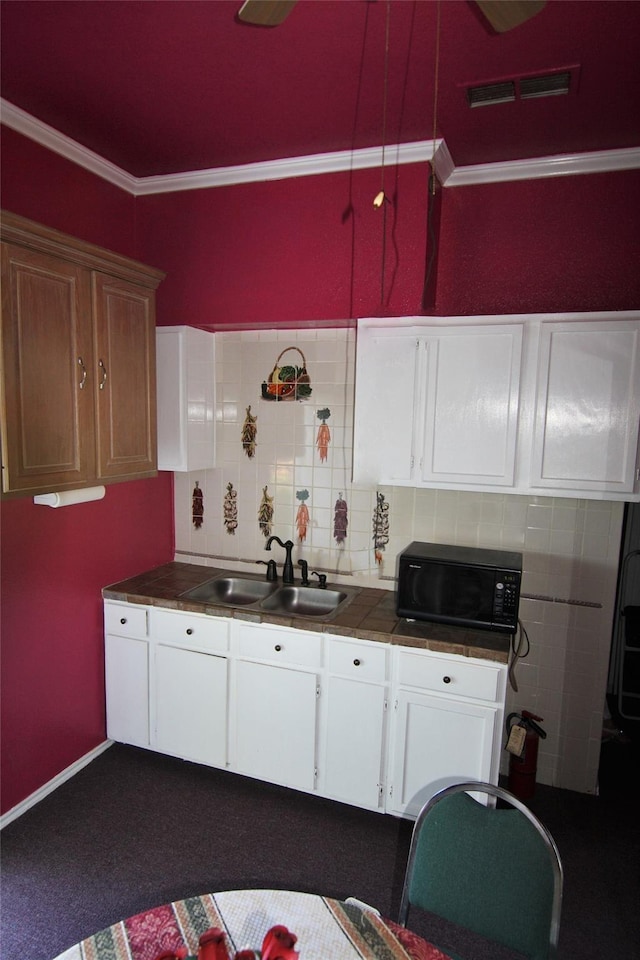 kitchen featuring tasteful backsplash, ornamental molding, sink, and white cabinets