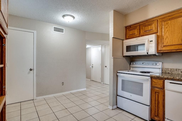 kitchen featuring a textured ceiling, light tile patterned flooring, dark stone counters, and white appliances