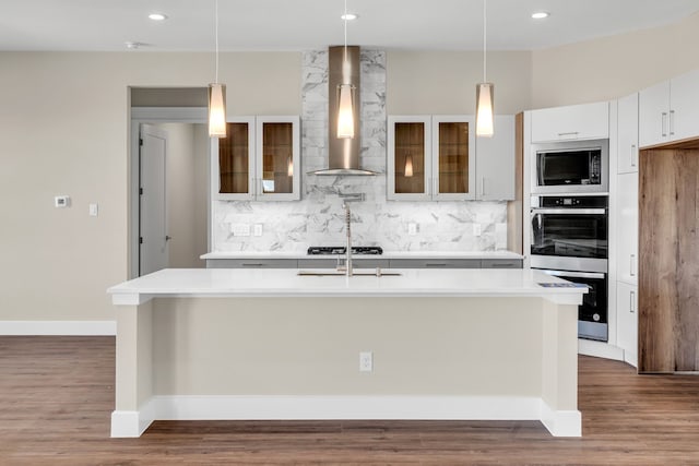 kitchen with stainless steel appliances, dark wood-style flooring, light countertops, wall chimney range hood, and decorative backsplash