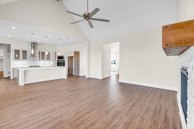 unfurnished living room with light wood-type flooring, ceiling fan, high vaulted ceiling, and a stone fireplace