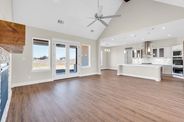 unfurnished living room featuring visible vents, french doors, wood finished floors, a stone fireplace, and a sink