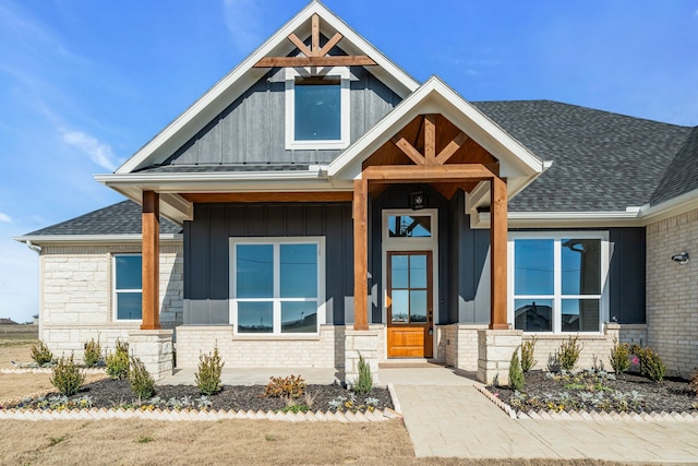 view of front of house with metal roof, a shingled roof, brick siding, board and batten siding, and a standing seam roof