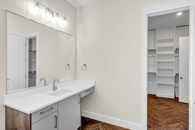 bathroom with a walk in closet, vanity, and baseboards