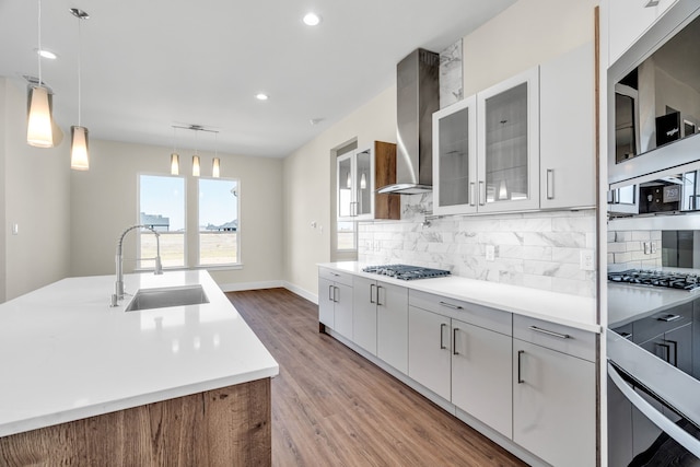 kitchen featuring a sink, light wood-style floors, light countertops, backsplash, and wall chimney exhaust hood