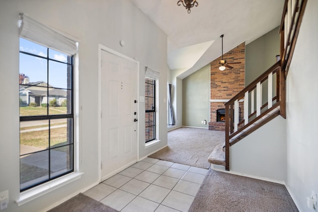 foyer with light carpet, ceiling fan, vaulted ceiling, and a brick fireplace