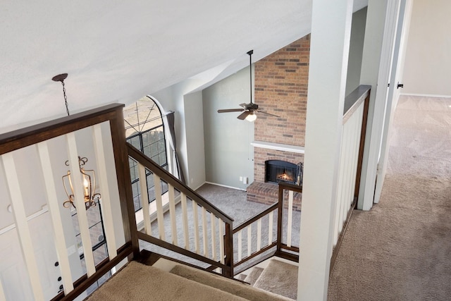 staircase featuring ceiling fan with notable chandelier, a brick fireplace, carpet floors, and vaulted ceiling