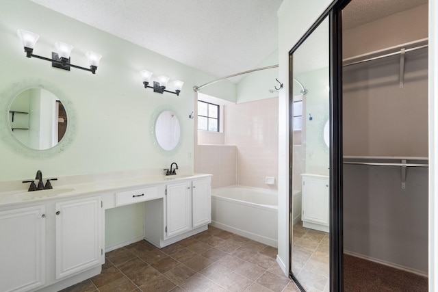 bathroom featuring vanity, a textured ceiling, and tiled shower / bath