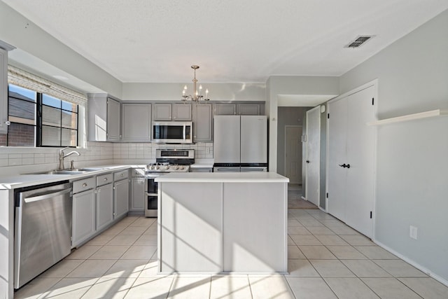 kitchen with gray cabinetry, a center island, sink, appliances with stainless steel finishes, and decorative light fixtures