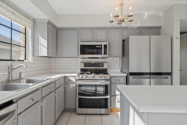 kitchen with appliances with stainless steel finishes, sink, light tile patterned floors, a notable chandelier, and gray cabinets