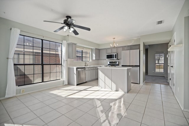 kitchen with a kitchen island, gray cabinets, light tile patterned floors, ceiling fan with notable chandelier, and appliances with stainless steel finishes