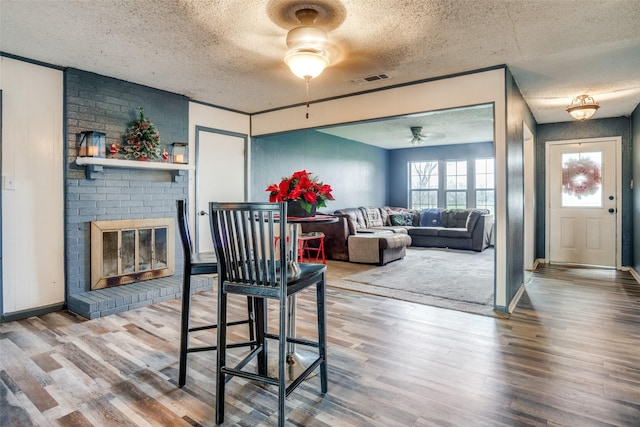 dining space featuring hardwood / wood-style flooring, ceiling fan, a textured ceiling, and a brick fireplace