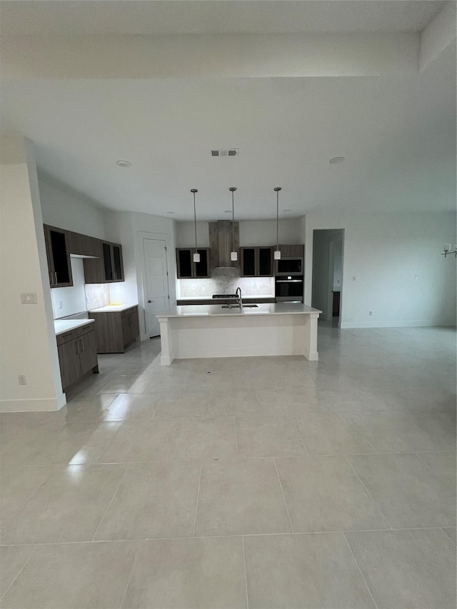 kitchen featuring dark brown cabinetry, sink, decorative light fixtures, a center island with sink, and light tile patterned flooring