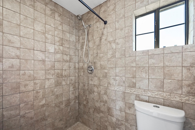 bathroom with a tile shower, tile walls, and toilet