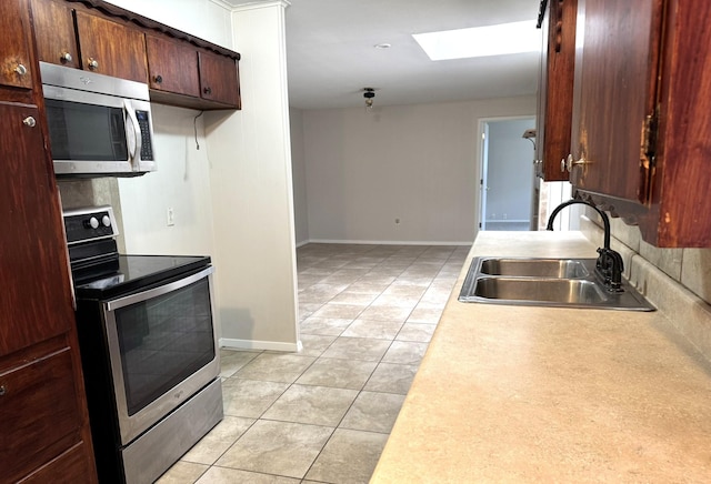 kitchen with appliances with stainless steel finishes, a skylight, tasteful backsplash, sink, and light tile patterned floors