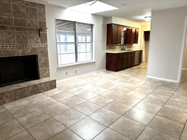 kitchen featuring a skylight, dark brown cabinets, sink, light tile patterned floors, and a tiled fireplace