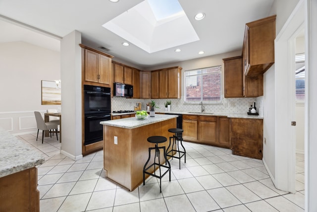 kitchen with a skylight, a center island, sink, a breakfast bar area, and black appliances