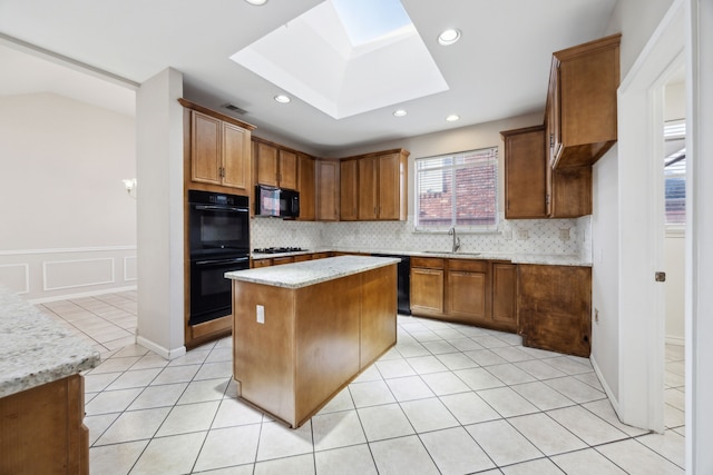 kitchen featuring light stone countertops, sink, light tile patterned floors, a kitchen island, and black appliances