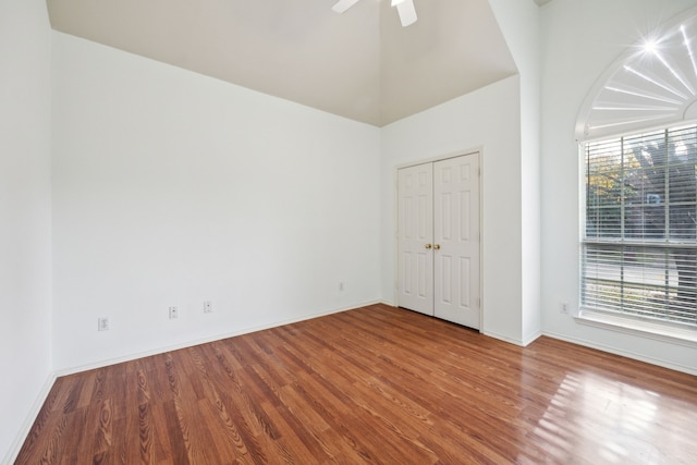 unfurnished bedroom featuring multiple windows, hardwood / wood-style floors, high vaulted ceiling, and ceiling fan