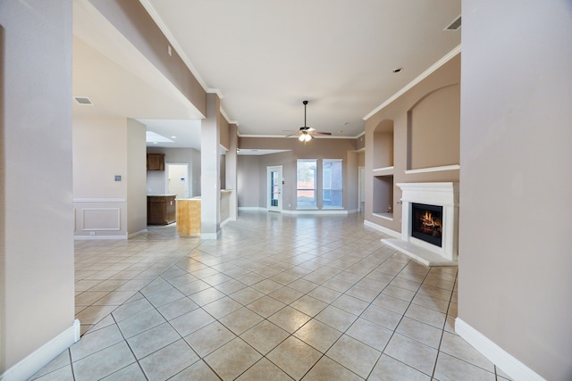 unfurnished living room featuring built in shelves, light tile patterned floors, ceiling fan, and crown molding