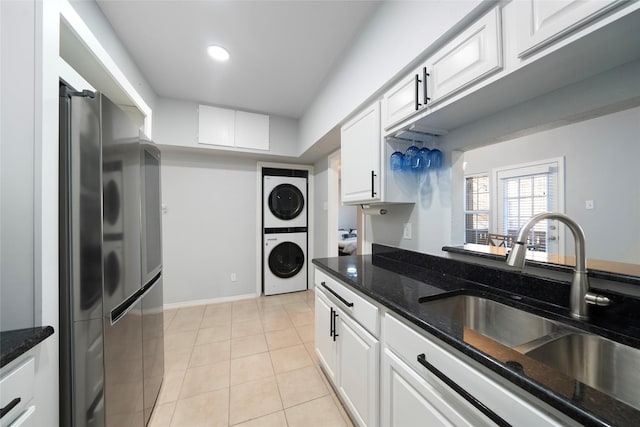 kitchen with dark stone counters, sink, stacked washer and dryer, stainless steel fridge, and white cabinetry