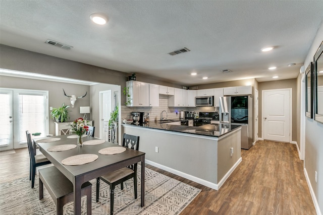 kitchen with sink, kitchen peninsula, stainless steel appliances, hardwood / wood-style floors, and white cabinets