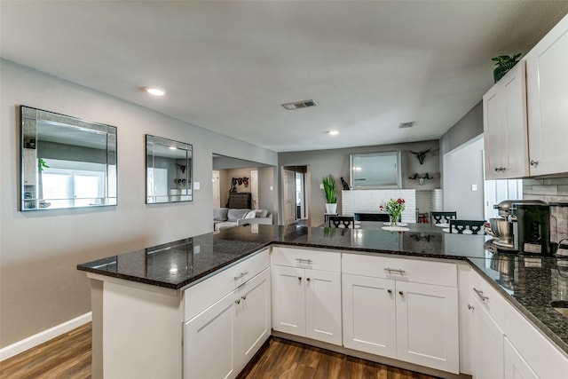 kitchen with decorative backsplash, kitchen peninsula, dark wood-type flooring, dark stone countertops, and white cabinets