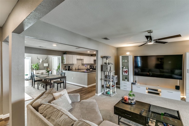 living room with ceiling fan, sink, and light colored carpet