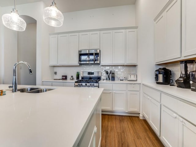 kitchen with pendant lighting, appliances with stainless steel finishes, sink, and white cabinets