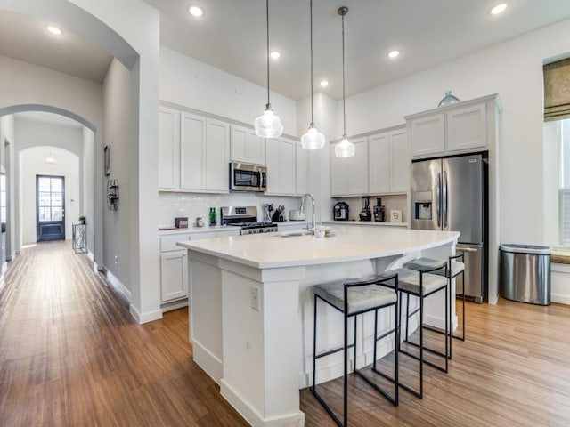 kitchen featuring appliances with stainless steel finishes, decorative light fixtures, white cabinetry, sink, and a kitchen island with sink