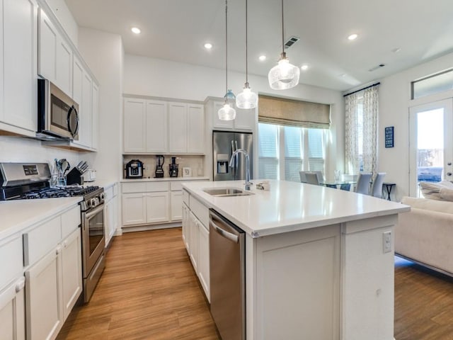 kitchen featuring pendant lighting, sink, a kitchen island with sink, stainless steel appliances, and white cabinets