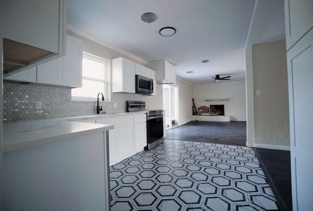 kitchen with ceiling fan, white cabinetry, stainless steel appliances, a fireplace, and ornamental molding