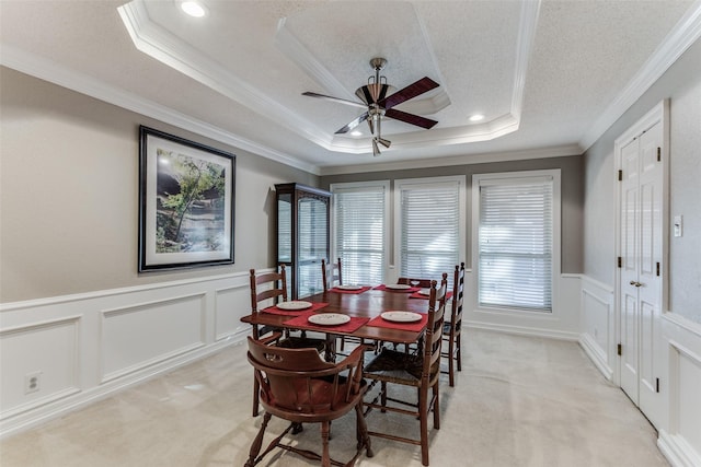 carpeted dining room with a textured ceiling, a raised ceiling, ceiling fan, and crown molding