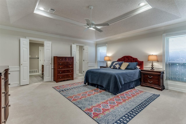 carpeted bedroom with ceiling fan, ensuite bathroom, a textured ceiling, a tray ceiling, and ornamental molding