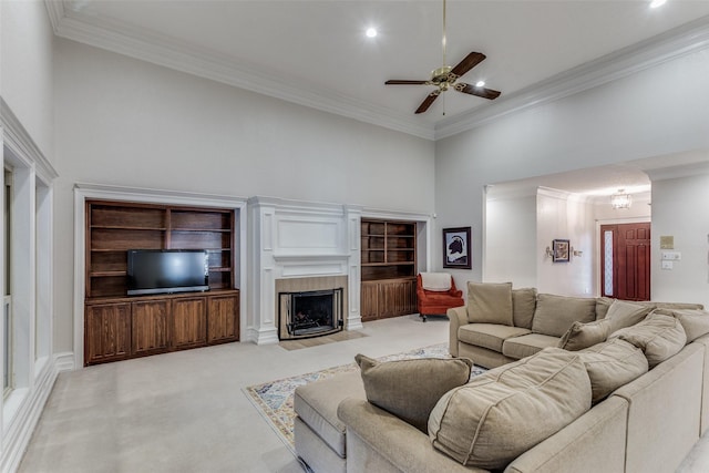 carpeted living room featuring a fireplace, a towering ceiling, ceiling fan, and ornamental molding