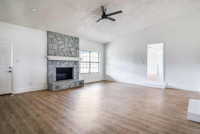 unfurnished living room with vaulted ceiling, ceiling fan, a textured ceiling, a fireplace, and wood-type flooring