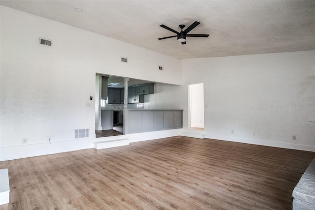 unfurnished living room with a textured ceiling, ceiling fan, a high ceiling, and hardwood / wood-style flooring