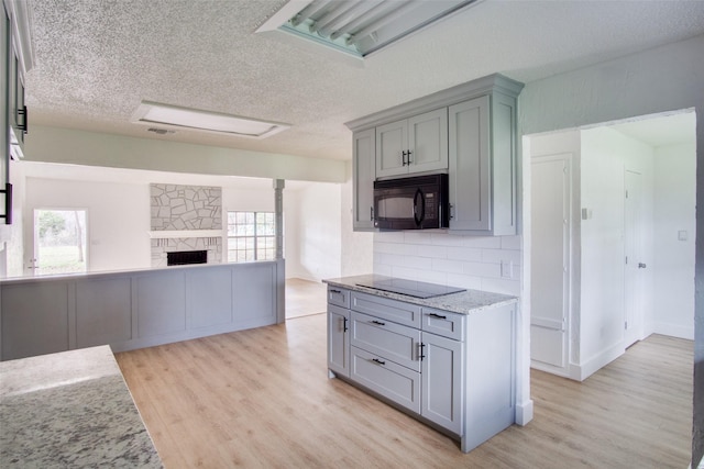 kitchen with light stone counters, light hardwood / wood-style flooring, decorative backsplash, a fireplace, and black appliances