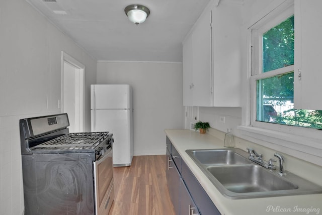 kitchen with stainless steel gas stove, white cabinetry, sink, white refrigerator, and dark wood-type flooring