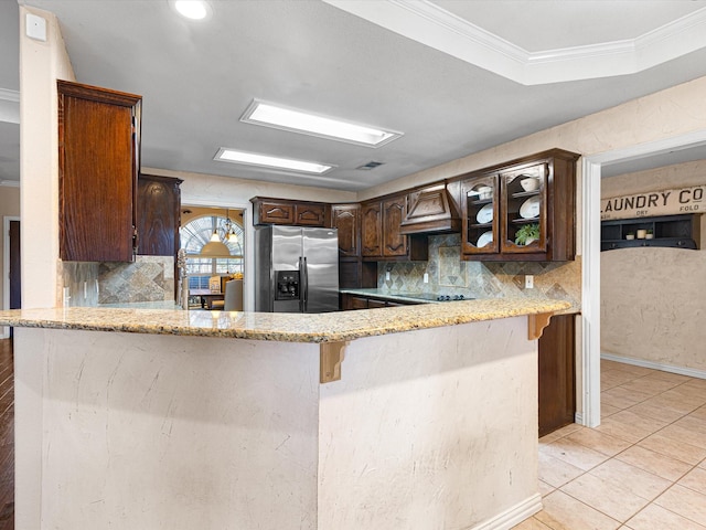 kitchen with kitchen peninsula, tasteful backsplash, ornamental molding, dark brown cabinetry, and stainless steel fridge with ice dispenser