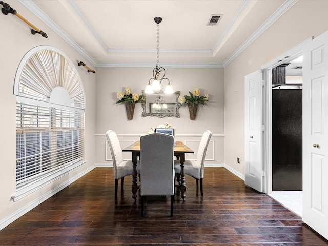 dining area with dark hardwood / wood-style flooring, a raised ceiling, ornamental molding, and an inviting chandelier