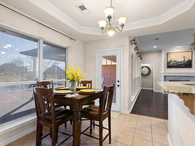 tiled dining space with ceiling fan with notable chandelier, a raised ceiling, and crown molding